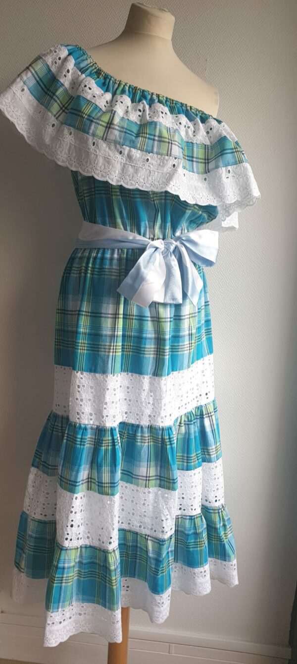 1.4Robe madras sur une couleur bleue turquoise cent pour cent coton. Dentelles et broderies anglaises ainsi que le col bardot sont autant de spécificités affirmant le caractère de la robe. Elle est de plus élastique à la taille conférant ainsi une entière liberté d'adaptabilité. Une ceinture en satin bicolore ajoute à sa valeur. Taille : S, M, L, XL.  Ce produit est entièrement confectionné dans les ateliers AnjeroCréation à Paris.