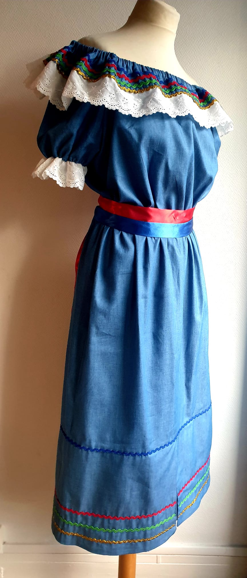16.2Robe carabela en bleu clair sur une tenue traditionnelle aux manches courtes. Elle est composée entièrement de coton. Sa confection se distingue par une élasticité à la taille, un maxi col bardot et de broderies anglaises aux êxtrèmités.Les Zigzags en bas de robe sont proposés dans quatre couleurs. Cette robe est livrée avec une ceinture bicolore rouge et bleue. Toutes les tailles sont proposées. Entièrement conçu et réalisé dans les ateliers AnjéroCréation à Paris.
