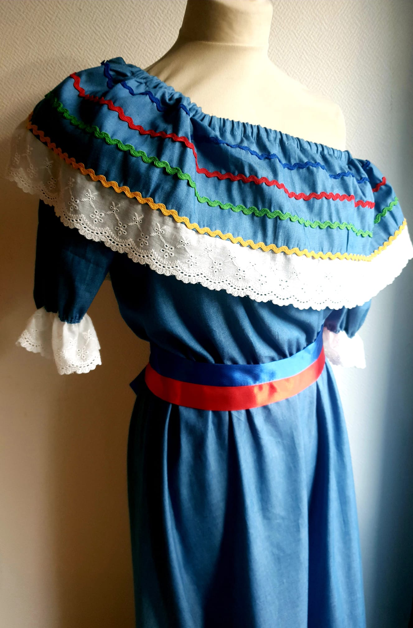 16.4Robe carabela en bleu clair sur une tenue traditionnelle aux manches courtes. Elle est composée entièrement de coton. Sa confection se distingue par une élasticité à la taille, un maxi col bardot et de broderies anglaises aux êxtrèmités.Les Zigzags en bas de robe sont proposés dans quatre couleurs. Cette robe est livrée avec une ceinture bicolore rouge et bleue. Toutes les tailles sont proposées. Entièrement conçu et réalisé dans les ateliers AnjéroCréation à Paris.