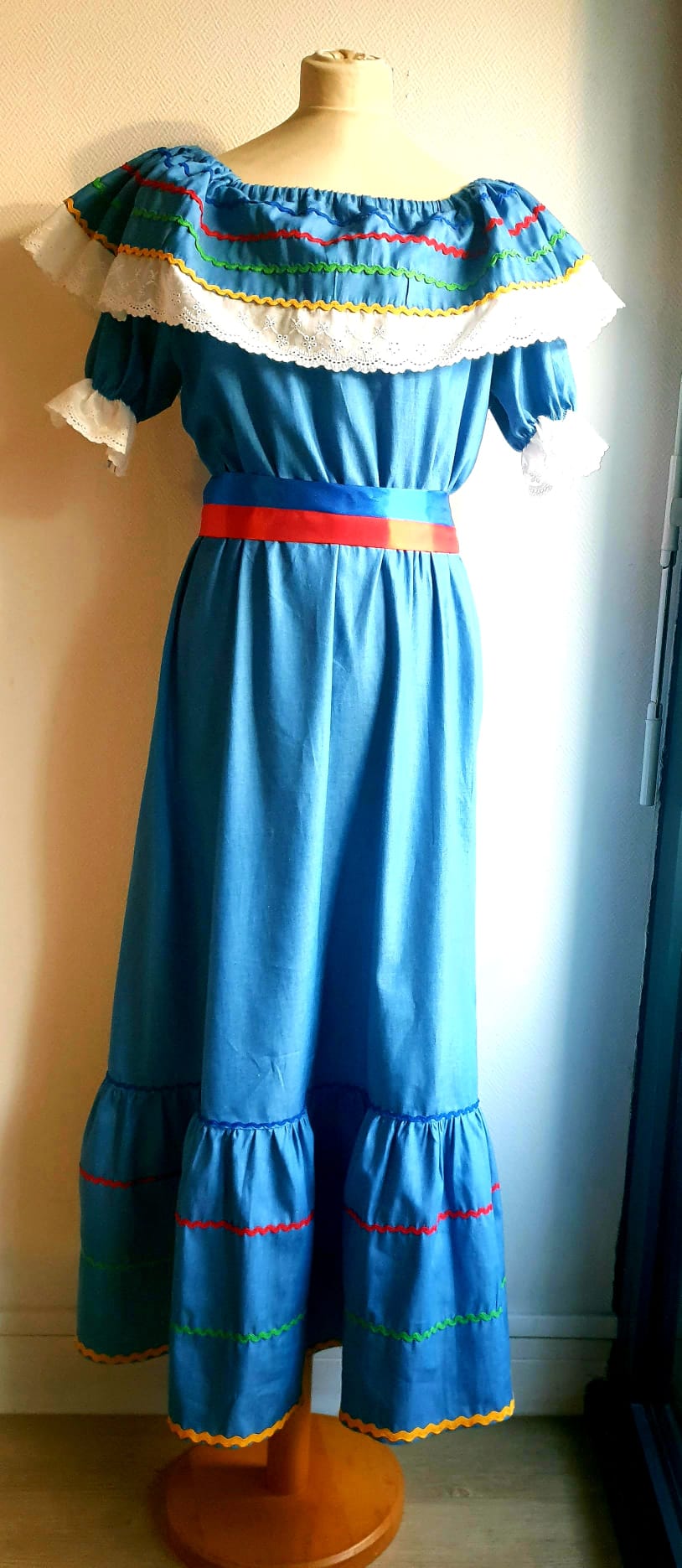 16.5Robe carabela en bleu clair sur une tenue traditionnelle aux manches courtes. Elle est composée entièrement de coton. Sa confection se distingue par une élasticité à la taille, un maxi col bardot et de broderies anglaises aux êxtrèmités.Les Zigzags en bas de robe sont proposés dans quatre couleurs. Cette robe est livrée avec une ceinture bicolore rouge et bleue. Toutes les tailles sont proposées. Entièrement conçu et réalisé dans les ateliers AnjéroCréation à Paris.