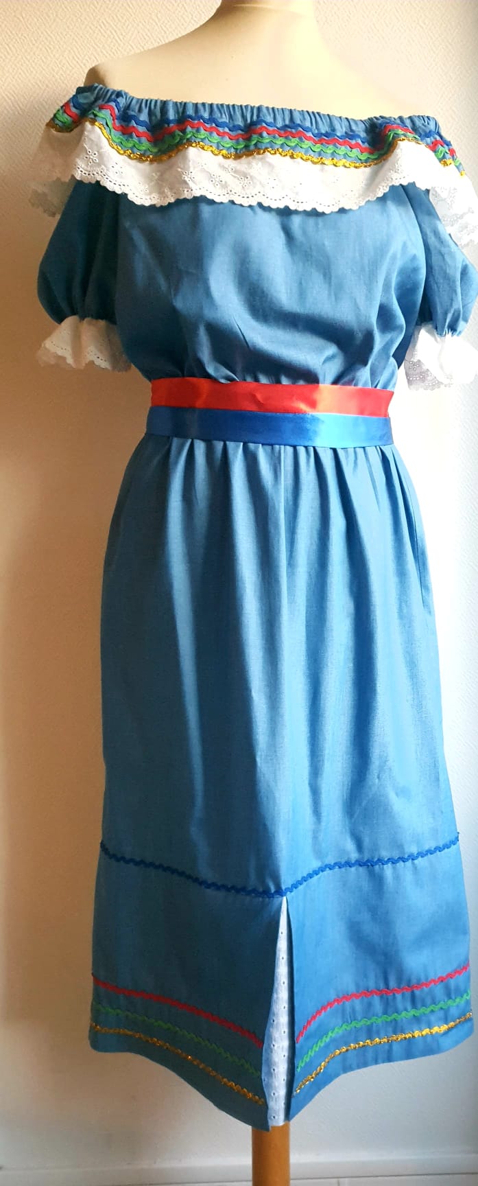 17.1Robe carabela en bleu clair sur une tenue traditionnelle aux manches courtes. Elle est composée entièrement de coton. Son style se distingue par une élasticité à la taille, un décoleté semi-plongeant, un maxi col bardot et de soyeuses broderies blanches anglaises aux êxtrèmités body. Les Zigzags ressérrés en bas et haut de robe proposés dans quatre couleurs de même que son fendu en son bas-milieu offrent ainsi une silhouette tout à fait originale. Cette robe est aussi livrée avec une ceinture bicolore rouge et bleue. Toutes les tailles sont proposées. Prix : 249.95€. Cette confection est entièrement conçue et réalisée dans les ateliers AnjéroCréation à Paris.