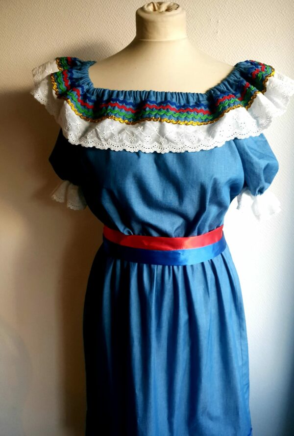 17.3Robe carabela en bleu clair sur une tenue traditionnelle aux manches courtes. Elle est composée entièrement de coton. Son style se distingue par une élasticité à la taille, un décoleté semi-plongeant, un maxi col bardot et de soyeuses broderies blanches anglaises aux êxtrèmités body. Les Zigzags ressérrés en bas et haut de robe proposés dans quatre couleurs de même que son fendu en son bas-milieu offrent ainsi une silhouette tout à fait originale. Cette robe est aussi livrée avec une ceinture bicolore rouge et bleue. Prix : 249.95€. Cette confection est entièrement conçue et réalisée dans les ateliers AnjéroCréation à Paris.