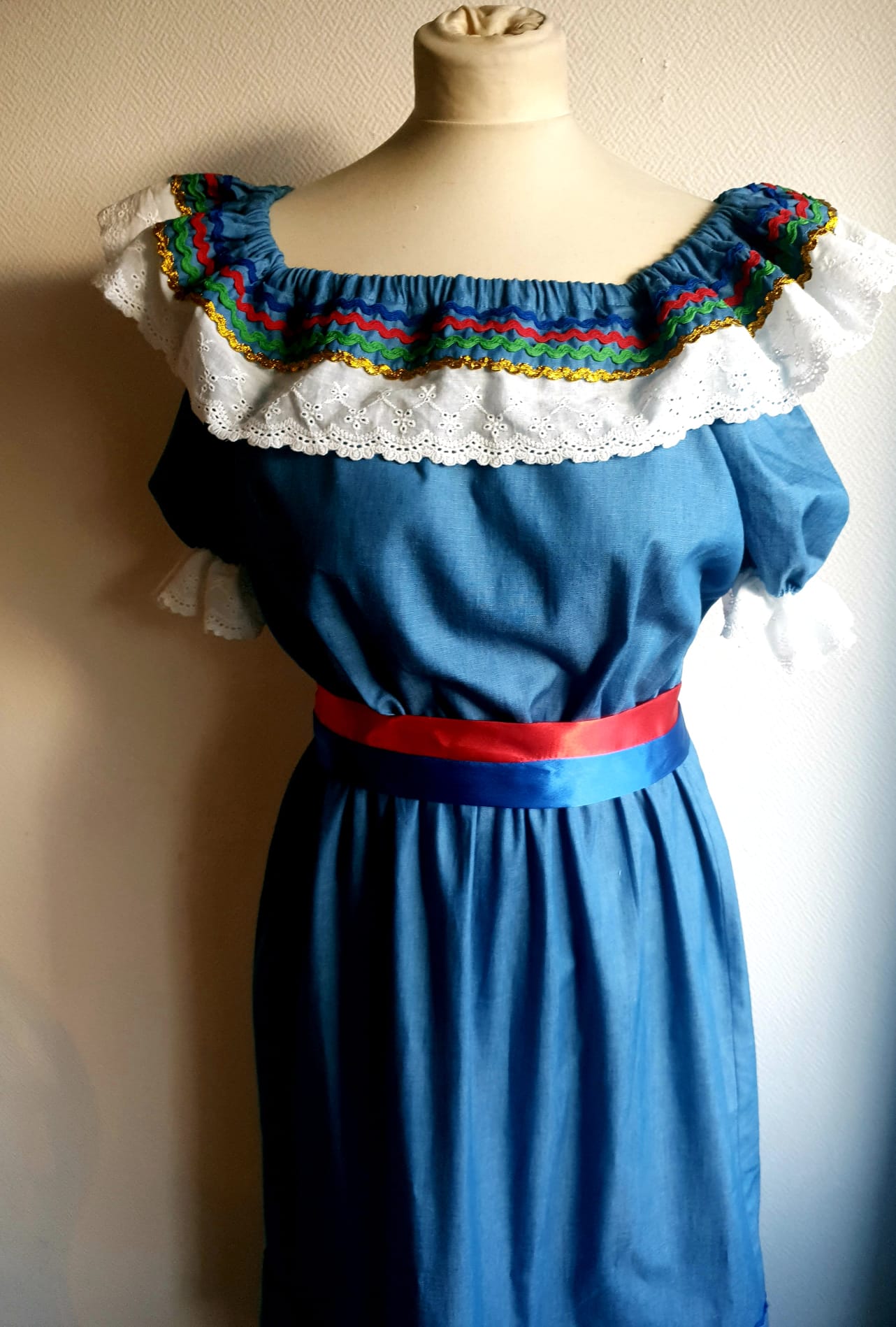 17.3Robe carabela en bleu clair sur une tenue traditionnelle aux manches courtes. Elle est composée entièrement de coton. Son style se distingue par une élasticité à la taille, un décoleté semi-plongeant, un maxi col bardot et de soyeuses broderies blanches anglaises aux êxtrèmités body. Les Zigzags ressérrés en bas et haut de robe proposés dans quatre couleurs de même que son fendu en son bas-milieu offrent ainsi une silhouette tout à fait originale. Cette robe est aussi livrée avec une ceinture bicolore rouge et bleue. Prix : 249.95€. Cette confection est entièrement conçue et réalisée dans les ateliers AnjéroCréation à Paris.