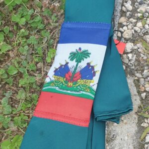 3.1Cravate de couleur bleue canard avec pochette et se caractérisant sur son devant par la distinction du drapeau Haïti. Prix : 23€.