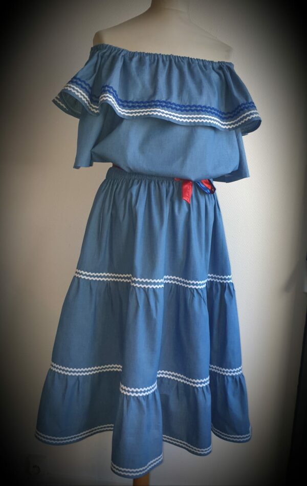 9.1Ensemble carabela en bleu avec manches courtes sur une tenue traditionnelle haïtienne. Cette confection  est pourvue de deux pièces appareillées d'une ceinture bicolore rouge et bleue. Cet ensemble est entièrement conçu et réalisé dans les ateliers AnjeroCreation à Paris. Taille : S, M, L, XL, XXl. Prix : 179.95€
