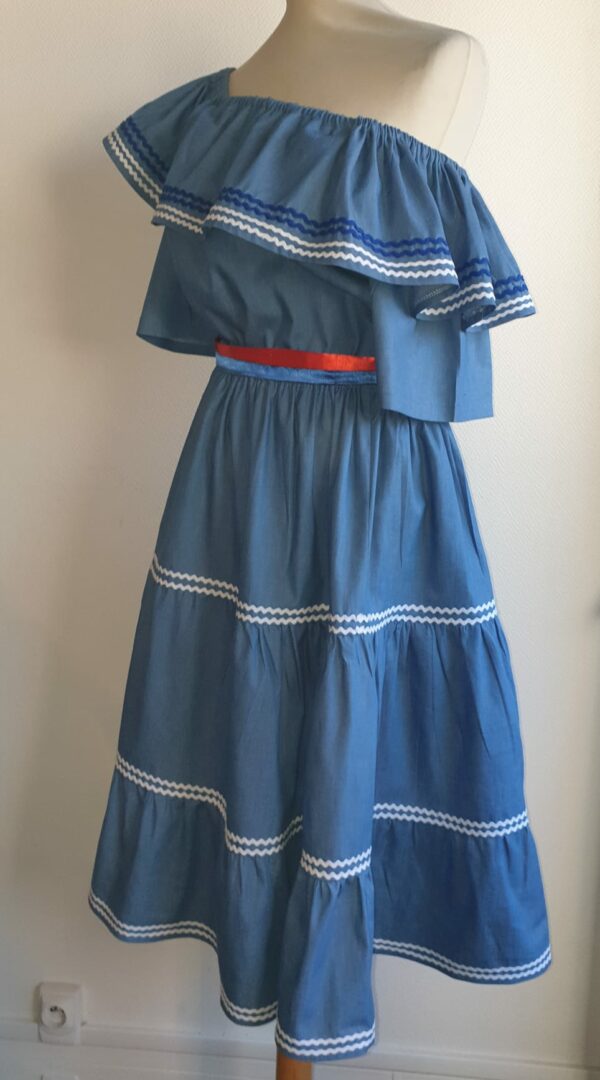 9.2Ensemble carabela en bleu avec manches courtes sur une tenue traditionnelle haïtienne. Cette confection  est pourvue de deux pièces appareillées d'une ceinture bicolore rouge et bleue. Cet ensemble est entièrement conçu et réalisé dans les ateliers AnjeroCreation à Paris. Taille : S, M, L, XL, XXl.