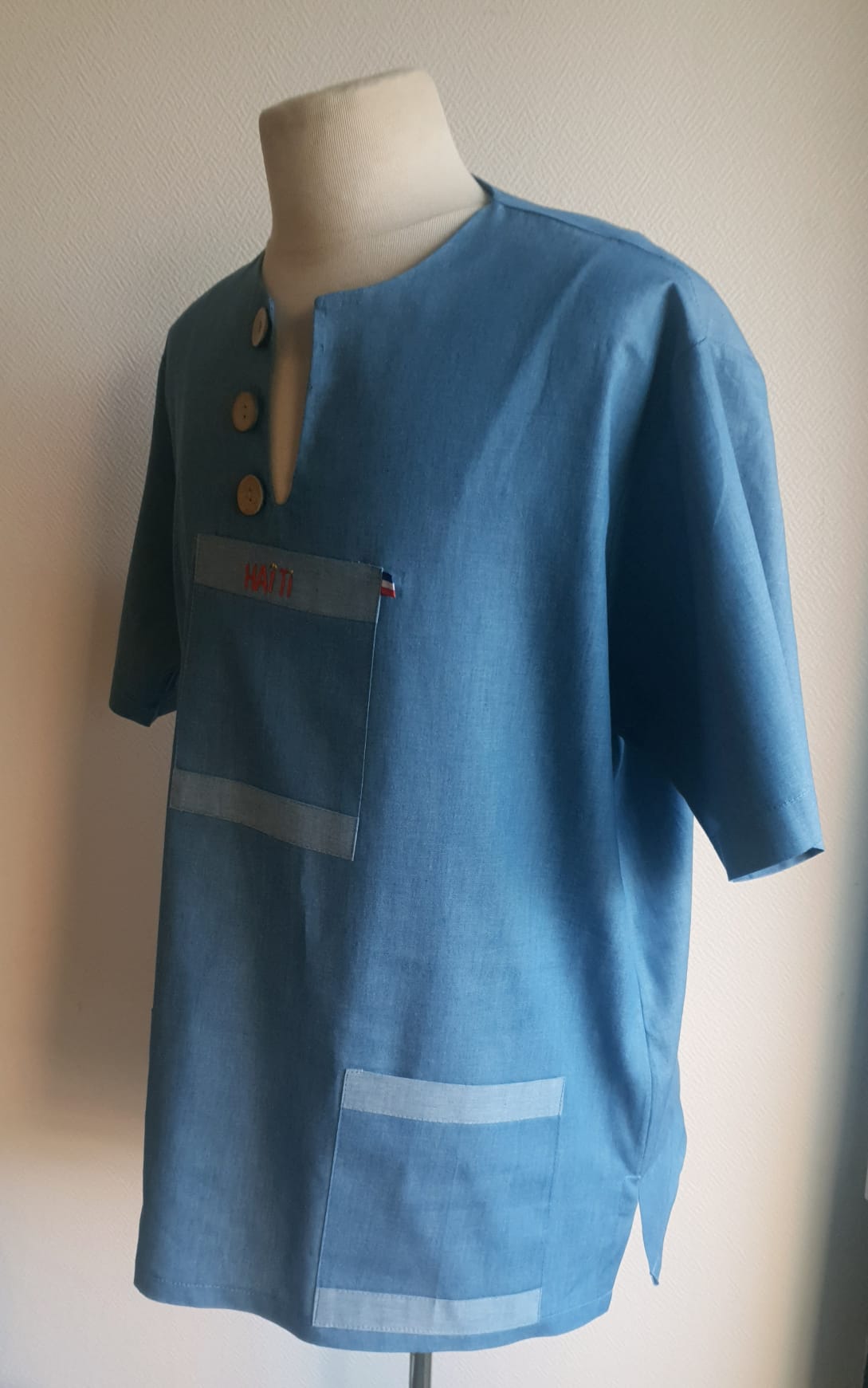 1.2Chemise homme carabela en manches courtees et en coton sur une tenue traditionnelle haïtienne sur un ton bleu ciel. Un col ras du coup arrondi et fendu au devant duquel, trois petits boutons en bois coco sont proposés. Deux poches simples et une poche ornée d'une petite broderie Haïti confèrent un style original à cette chemise. Prix : 69.95€.