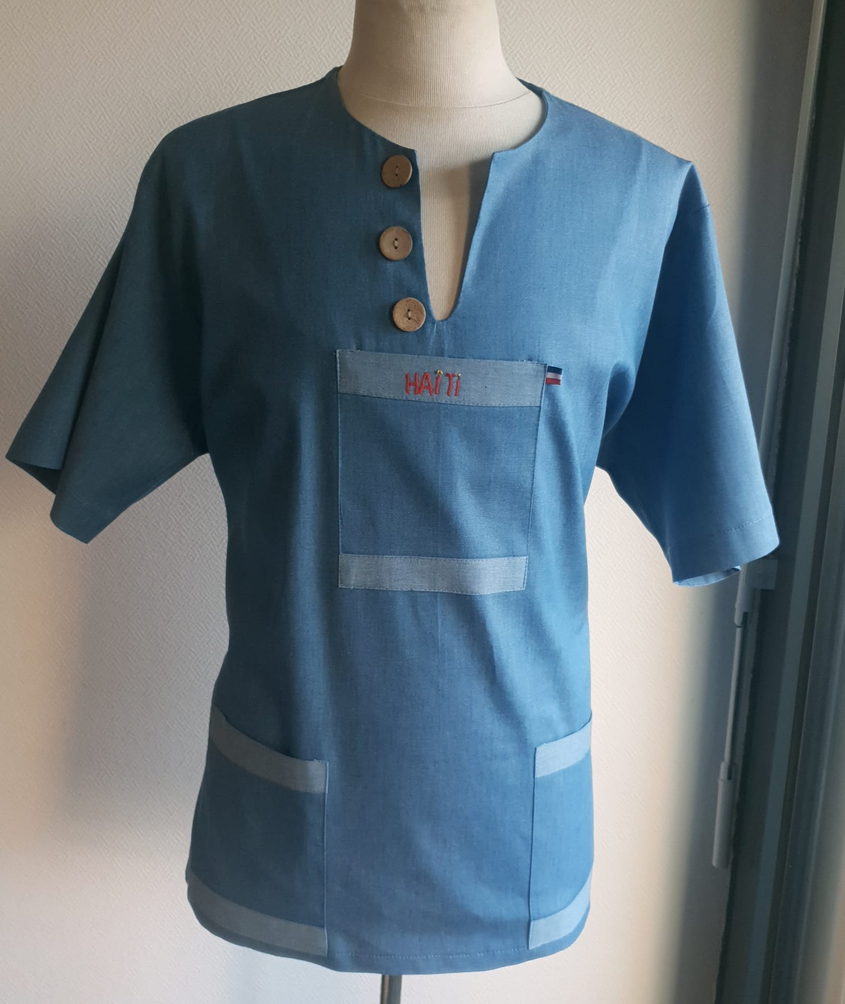 1.3Chemise homme carabela en manches courtees et en coton sur une tenue traditionnelle haïtienne sur un ton bleu ciel. Un col ras du coup arrondi et fendu au devant duquel, trois petits boutons en bois coco sont proposés. Deux poches simples et une poche ornée d'une petite broderie Haïti confèrent un style original à cette chemise. Prix : 69.95€.