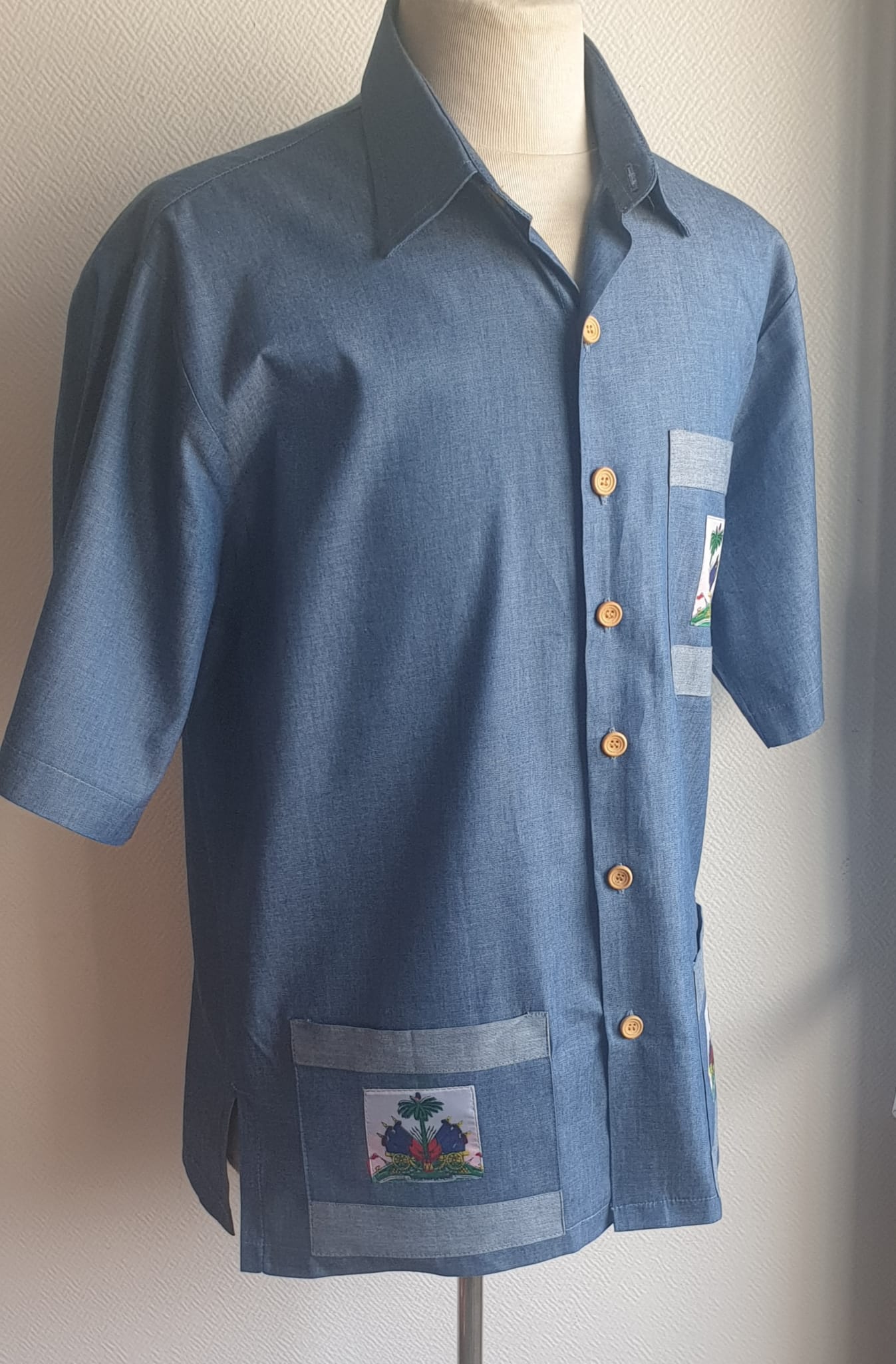 4.5Chemise carabela en tissu cent pour cent coton. Trois poches dont une munie du drapeau haïtien. Tissu travaillé à la main avec une petite poche cousue sur manche courte. Un Col classique a été choisi pour ce modèle avec un ensemble linéaire de boutons en bois coco verticaux. Cette chemise est entièrement conçue et réalisée dans les ateliers AnjeroCréation à Paris. Prix : 79.95€.