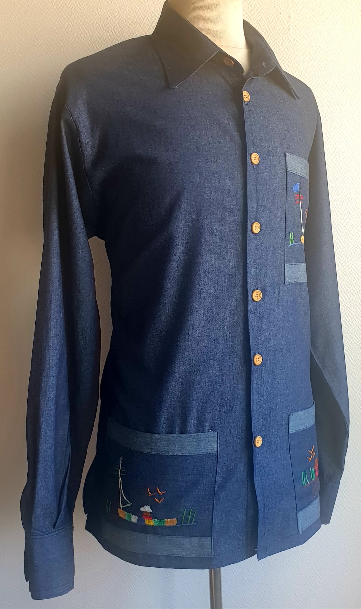 5.1Chemise carabela traditionnelle haïtienne en bleu marine. Trois poches brodées main. Ensemble linéaire de boutons verticaux et centraux en bois coco. Tissu cent pour cent coton. Cette chemise est entièrement conçue et réalisée dans les ateliers AnjeroCréation à Paris. Prix : 79.95€.