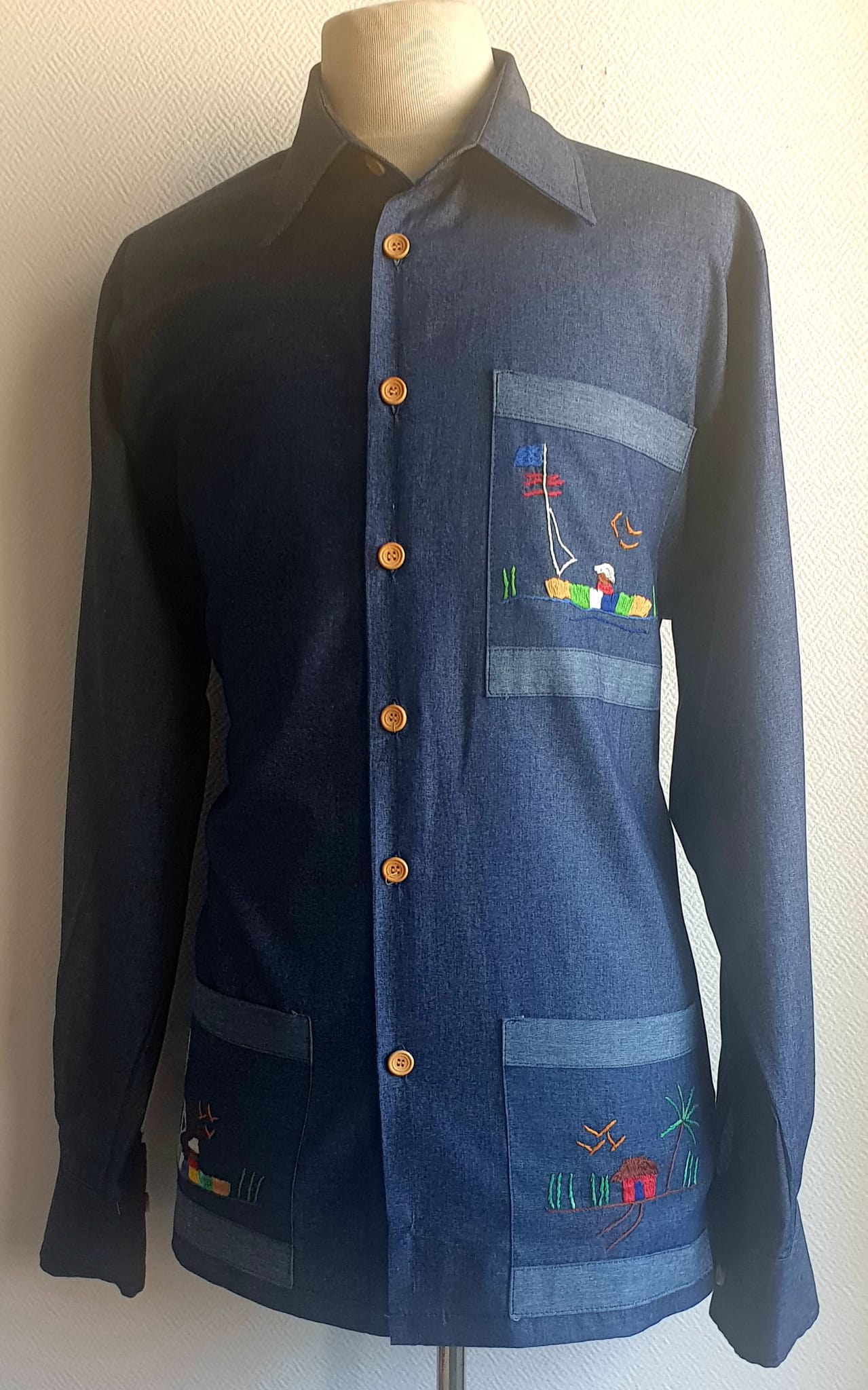 5.2Chemise carabela traditionnelle haïtienne en bleu marine. Trois poches brodées main. Ensemble linéaire de boutons verticaux et centraux en bois coco. Tissu cent pour cent coton. Cette chemise est entièrement conçue et réalisée dans les ateliers AnjeroCréation à Paris. Prix : 79.95€.