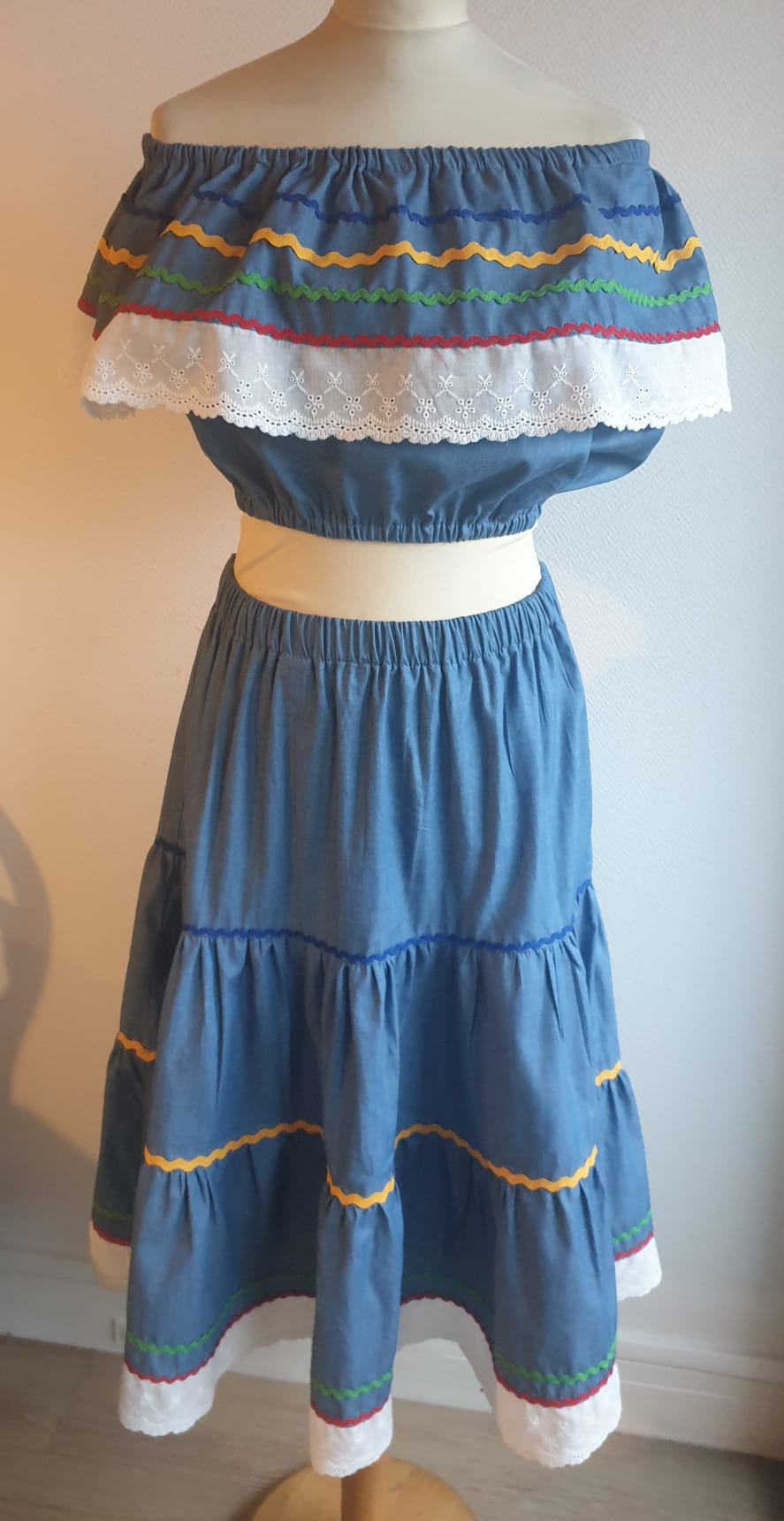 35.2Ensemble carabela bleu foncé sur une tenue traditionnelle haïtienne. Deux pièces. Jupe longue et élastique à la taille. Le corsage dispose au bas d'une appréciable élasticité, pouvant ainsi s'adapter à toutes les formes de buste. Les broderies blanches en dentelles anglaises sont cousues au bas du col bardot. Cette production est livrée avec, de surcroît, une grande ceinture aux couleurs du drapeau haïtien. Taille : S, M, L, XL, XXL. Prix : 239.95€. Création artisanale. Entièrement conçu et réalisé aux ateliers AnjeroCréation à Paris.