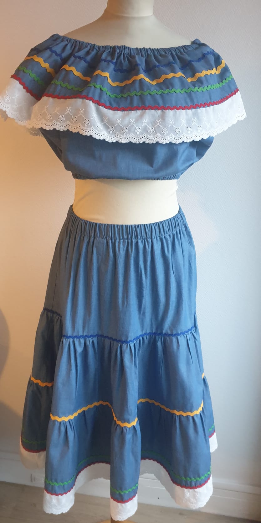 35.3Ensemble carabela bleu foncé sur une tenue traditionnelle haïtienne. Deux pièces. Jupe longue et élastique à la taille. Le corsage dispose au bas d'une appréciable élasticité, pouvant ainsi s'adapter à toutes les formes de buste. Les broderies blanches en dentelles anglaises sont cousues au bas du col bardot. Cette production est livrée avec, de surcroît, une grande ceinture aux couleurs du drapeau haïtien. Taille : S, M, L, XL, XXL. Prix : 239.95€. Création artisanale. Entièrement conçu et réalisé aux ateliers AnjeroCréation à Paris.