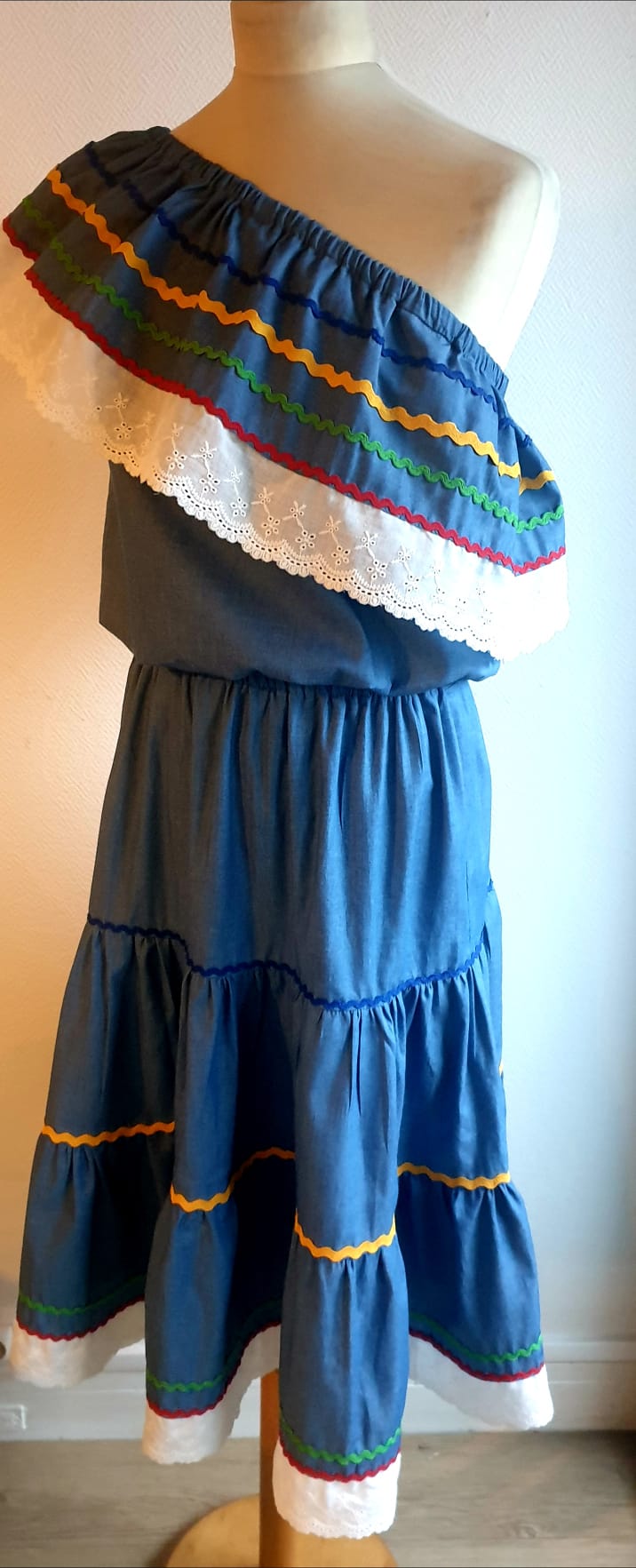 35.4Ensemble carabela bleu foncé sur une tenue traditionnelle haïtienne. Deux pièces. Jupe longue et élastique à la taille. Le corsage dispose au bas d'une appréciable élasticité, pouvant ainsi s'adapter à toutes les formes de buste. Les broderies blanches en dentelles anglaises sont cousues au bas du col bardot. Cette production est livrée avec, de surcroît, une grande ceinture aux couleurs du drapeau haïtien. Taille : S, M, L, XL, XXL. Prix : 239.95€. Création artisanale. Entièrement conçu et réalisé aux ateliers AnjeroCréation à Paris.