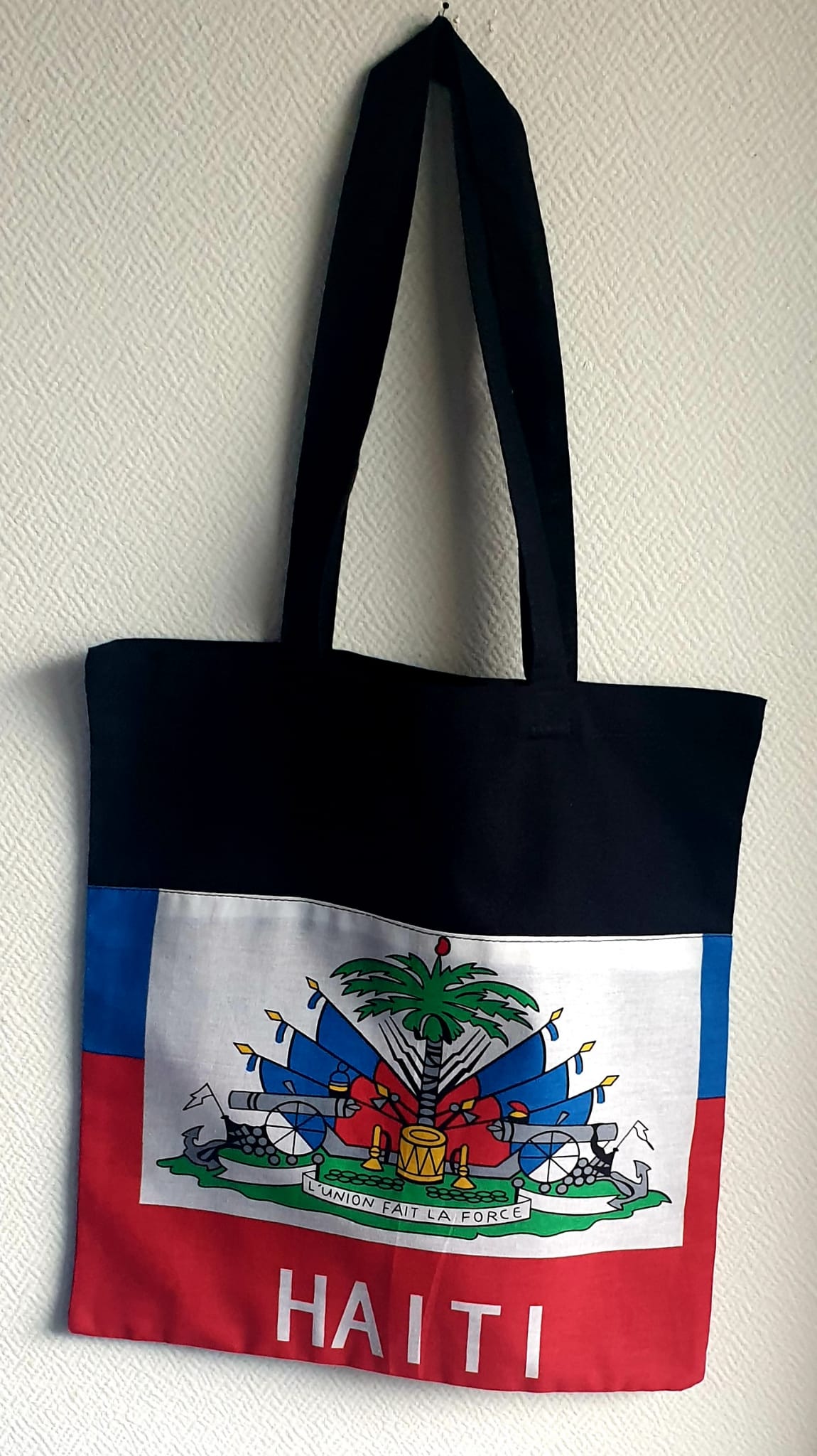 1.1Tote-bag en coton sur un extérieur bleu rouge orné du drapeau haïtien. Son intérieur est tout en noir. Ce produit es muni d'une élégante anse de bonne hauteur aux fins de facilité son port. Entièrement conçu et réalisé aux ateliers AnjeroCréation à Paris. Prix : 19,95€.