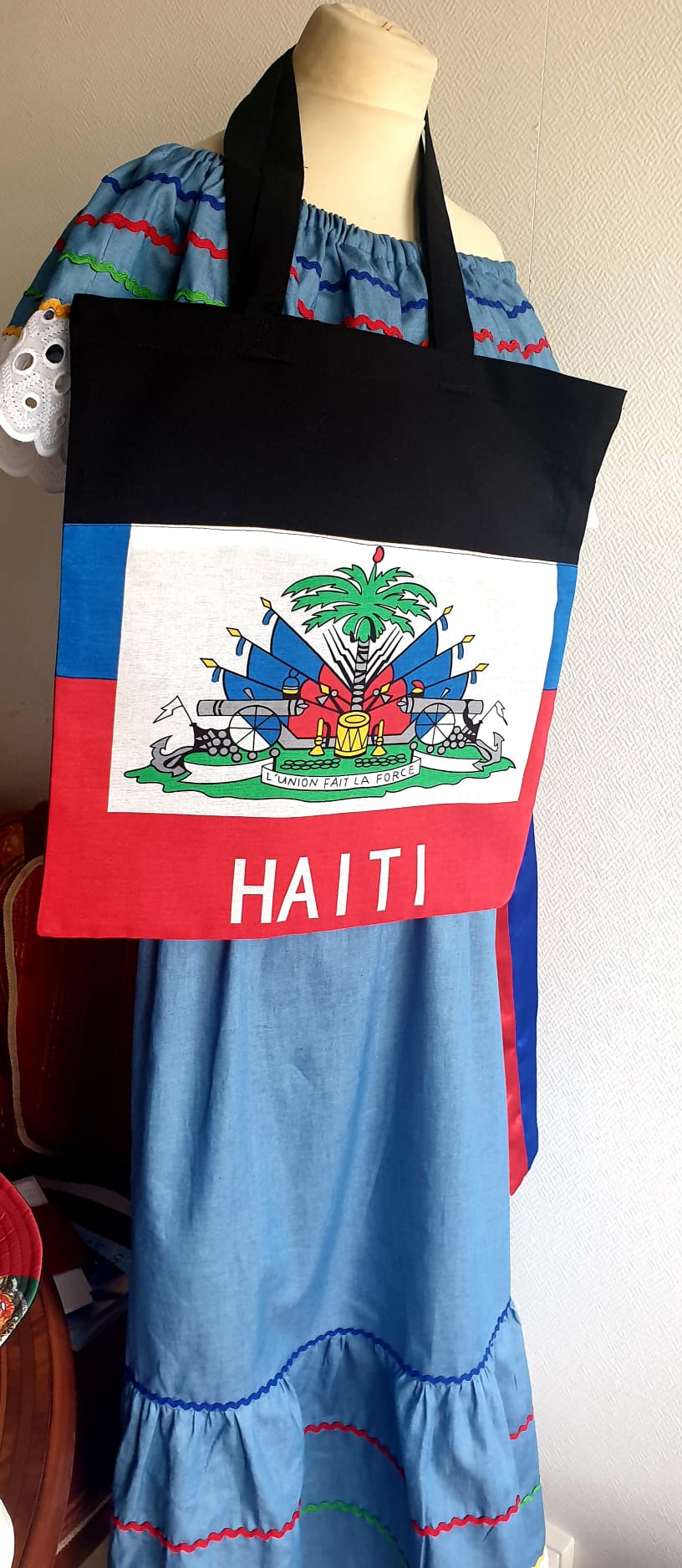 1.2Tote-bag en coton sur un extérieur bleu rouge orné du drapeau haïtien. Son intérieur est tout en noir. Ce produit es muni d'une élégante anse de bonne hauteur aux fins de facilité son port. Entièrement conçu et réalisé aux ateliers AnjeroCréation à Paris. Prix : 19,95€.