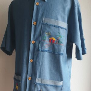 21.1Chemise Carabela traditionnelle haïtienne avec son col classique. Cinq boutons en bois sont disposés sur le devant en ligne centrale. Trois poches brodées à la main avec sur la poche droite l'image traditionnelle d'un petit homme. Une poche miniaturisée se distingue sur la demie manche gauche.