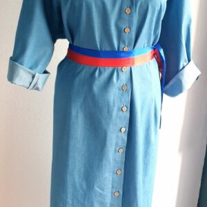 20.1 Robe Carabela longue sur une tenue traditionnelle. Style chemisier bleu avec 2 pinces devant , derrière. Col et pied de col. Cette confection se distingue par une boutonnière en bois coco sur le milieu de haut en bas. Une ceinture bleue rouge est également proposée. Taille : S, M, L, XL, XXL. Prix : 159.95€. La robe est entièrement conçue et réalisée aux ateliers AnjeroCréation à Paris.