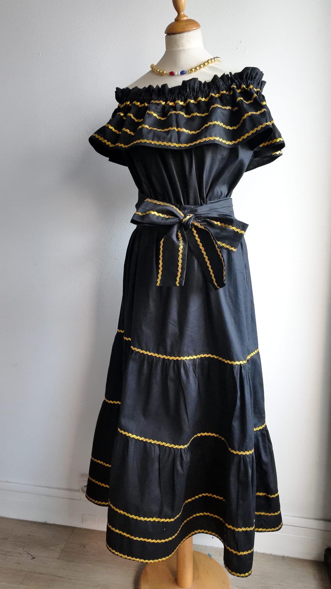 26.1Robe carabela en noire, tissu popeline de coton. Élastique à la taille. Zigzags dorés. L'ajout d'une ceinture décorée marque la taille et apporte une touche harmonieuse à la silhouette. Modèle entièrement conçu et réalisé aux ateliers AnjeroCréation à Paris. Prix : 329.95€