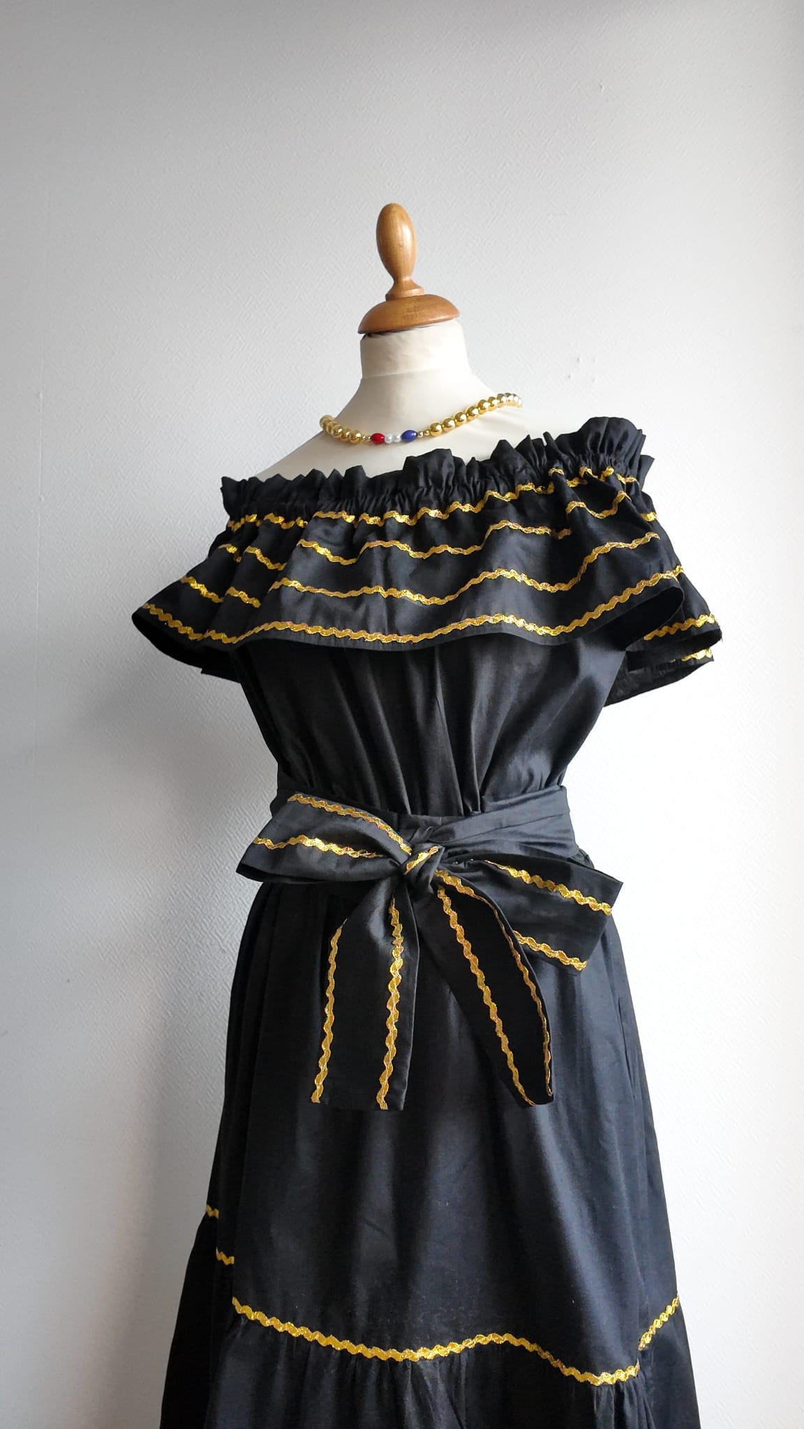 26.2Robe carabela en noire, tissu popeline de coton. Élastique à la taille. Zigzags dorés. L'ajout d'une ceinture décorée marque la taille et apporte une touche harmonieuse à la silhouette. Modèle entièrement conçu et réalisé aux ateliers AnjeroCréation à Paris. Prix : 329.95€