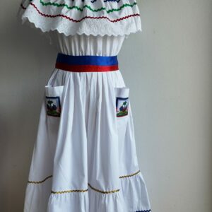 27.1Robe carabela en blanc, tissu popeline de coton. Élastique à la taille. Deux poches. Zigzags aux couleurs du drapeau haïtien. Dentelles décorées de broderies anglaises. La couleur de la robe fait merveilleusement bien ressortir la ceinture bleue, rouge. Peut être porté avec ou sans jupon. Modèle entièrement conçu et réalisé aux ateliers AnjeroCréation à Paris. Taille S, M, L, XL, XXL. Prix 359.95€